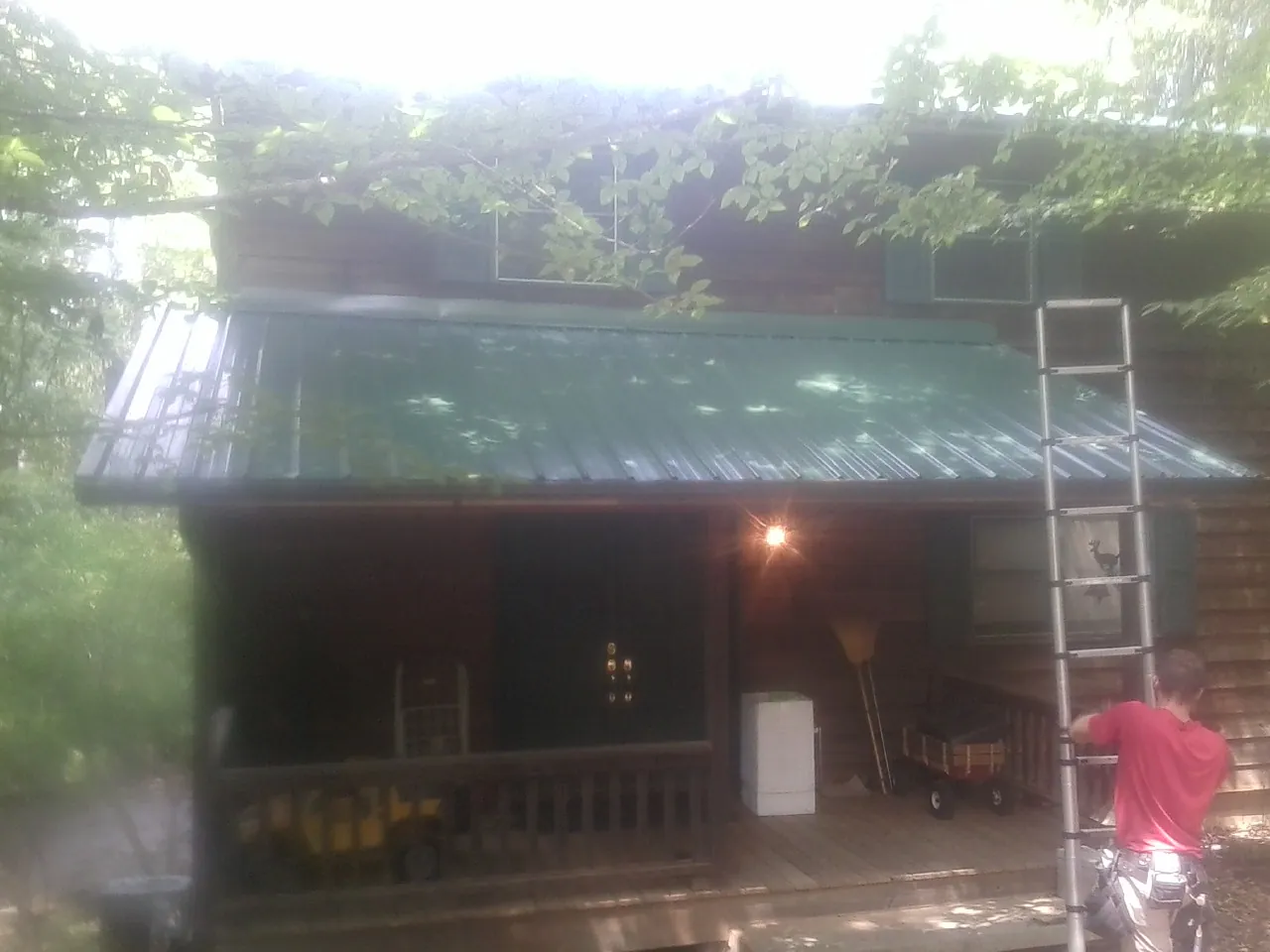 Worker on a ladder at the green porch roof of a wooded cabin in Aurora